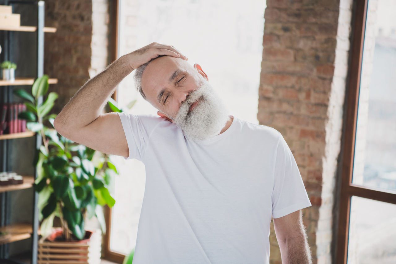 Photo of handsome smiling good mood grandfather stretching neck with closed eyes exercising at home quarantine,Photo of handsome smiling good mood grandfather stretching neck 