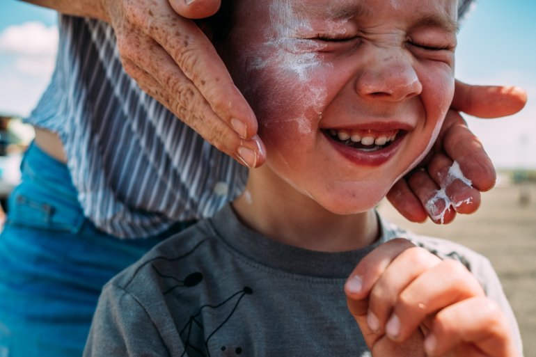 Mutter cremt ihren Sohn mit Sonnencreme ein